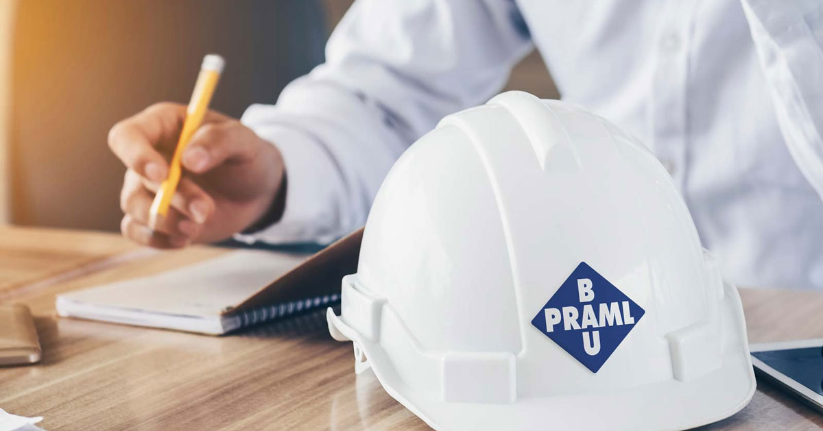 Ein Helm mit Praml Bau Logo auf einem Schreibtisch vor einem Mitarbeitenden